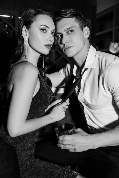 Elegant man holding glass of whiskey near girlfriend in dress in bar  - Fotoğraf, Görsel