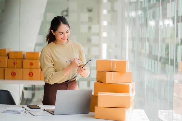 Small business startups, SME owners, Asian women entrepreneurs Successfully working with boxes and checking online orders with a laptop to prepare. Sell to customers. Online SME Business Ideas - Fotoğraf, Görsel