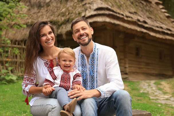 Happy family in Ukrainian national clothes sitting on bench outdoors - Zdjęcie, obraz