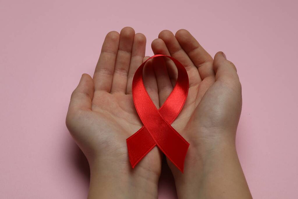 Little girl holding red ribbon on pink background, closeup. AIDS disease awareness - Fotoğraf, Görsel