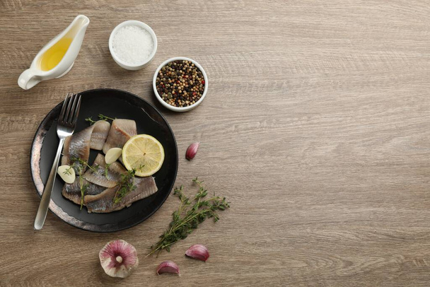Delicious salted herring fillets served with lemon, thyme and garlic on wooden table, flat lay. Space for text - Φωτογραφία, εικόνα