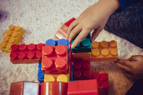 Κοντινό πλάνο του παιδιού παίζει με πλαστικά μπλοκ. Δημιουργικό παιδί χτίζει κάτι με μπλοκ παιχνιδιών στο χαλί. - Φωτογραφία, εικόνα
