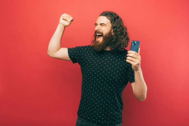 A happy bearded man is being very excited while holding his phone - Foto, imagen