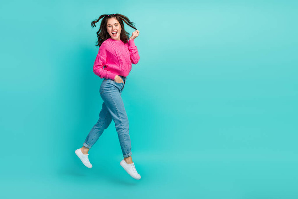 Full size photo of cute girl with wavy hairdo pink pullover jeans sneakers hand in pocket touch hair isolated on teal color background. - Фото, изображение