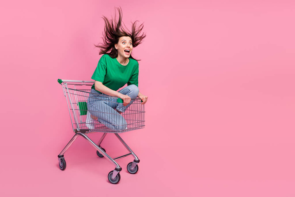 Full size portrait of overjoyed carefree girl sit inside market trolley look empty space isolated on pink color background. - Foto, Imagem