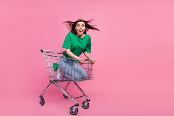 Full length portrait of cheerful overjoyed girl sitting inside supermarket trolley isolated on pink color background. - Foto, afbeelding