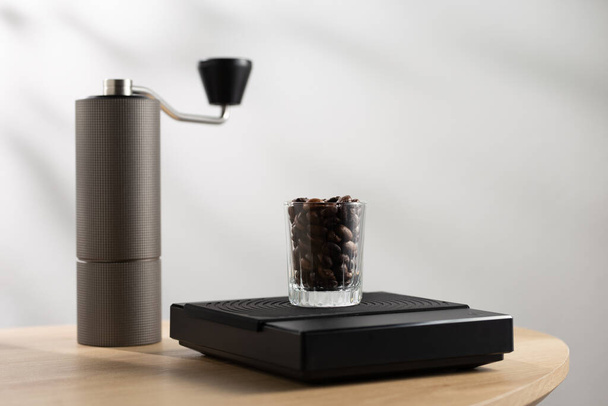 Dark roasted coffee beans in a clear glass on a digital scale and a Manual coffee grinder - Fotografie, Obrázek