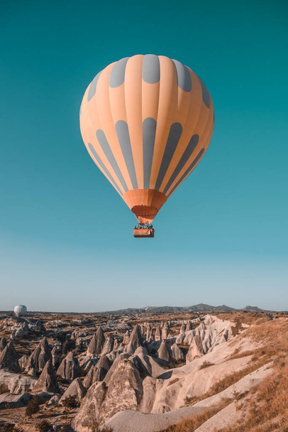 One orange hot air balloon against blue morning sky flight above mountains. Cappadocia at sunrise. Goreme national park, Turkey. Vintage retro orange blue toning filter. Tourism, travel, holidays - Fotoğraf, Görsel