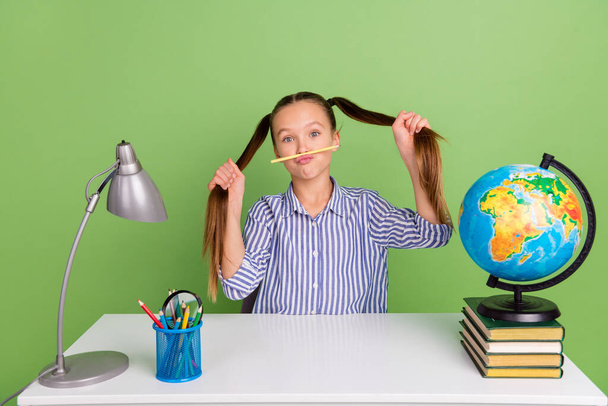 Photo of pretty funky small schoolkid dressed striped uniform tails fooling sitting desktop isolated green color background. - Фото, зображення