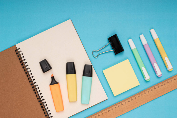 Блокнот, кольорові олівці, лінійка, нотатка паперу і затискач. повернутися до школи. Ізольований синій фон
 - Фото, зображення
