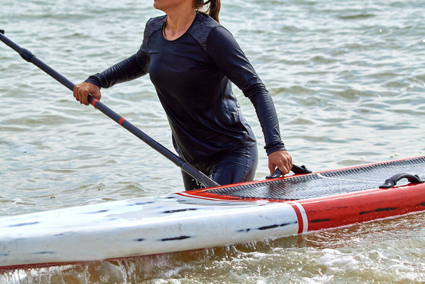 Ελκυστική νεαρή κοπέλα κρατήσει sup board στέκεται στη θάλασσα - Φωτογραφία, εικόνα