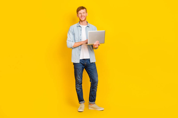 Full length photo of young smiling happy guy hold laptop programmer professional invent new app isolated on yellow color background. - 写真・画像