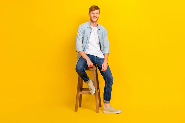 Full size photo of young creative handsome guy wear casual clothes sitting chair waiting end lesson isolated on yellow color background. - Photo, image