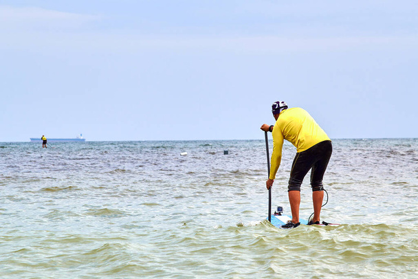Athletic man paddling on stand up paddle board (paddleboard, SUP) on sea. Stand up paddle boarding - awesome active recreation in nature. Back view. - Fotografie, Obrázek