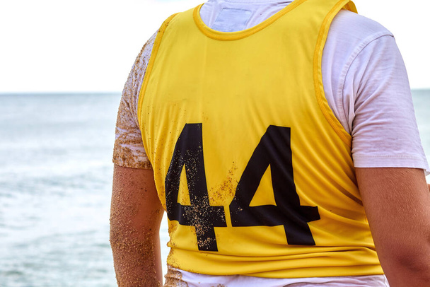 Вид ззаду чоловічий спортсмен у жовтій футболці з номером 44 стоїть біля моря
 - Фото, зображення