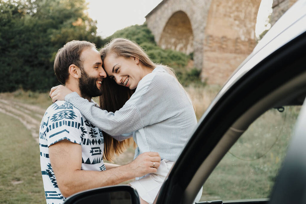 Caucasian man and woman hugging on hood of car, middle-aged couple enjoying road trip together - Foto, Imagem