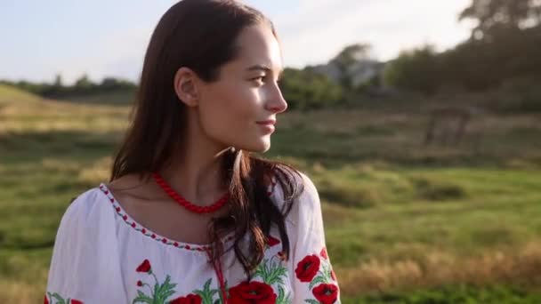 Portrait of young Ukrainian smiling woman in traditional national embroidered shirt and necklace on meadow. Ethnic ukrainian national clothes style, embroidered shirt. - Video
