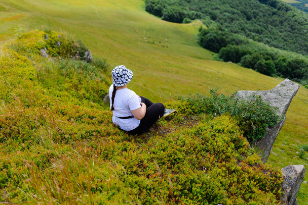 High angle view of a woman sitting on the grass in the mountains and observing a beautiful landscape - Foto, Bild