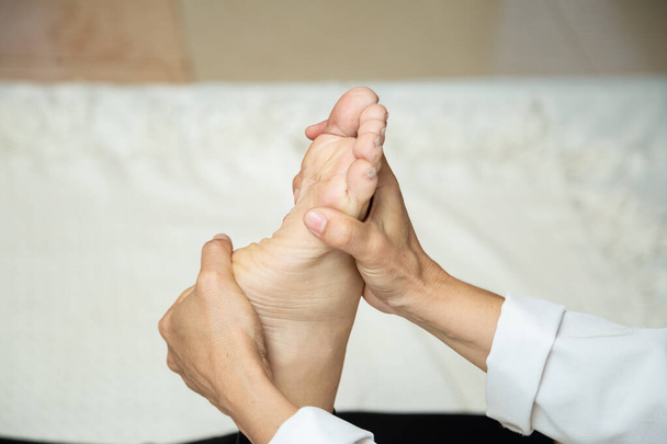 Closeup of massage therapist hands applying therapeutic massage to a patient's foot. - Photo, image
