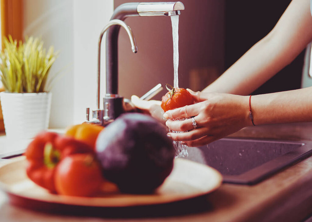 Woman washing tomatoes in kitchen sink close up. - 写真・画像