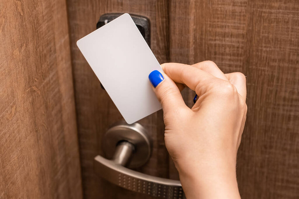 Woman hand puts key card to panel opening hotel room door. Female person with blue nails opening door  - Foto, Imagen