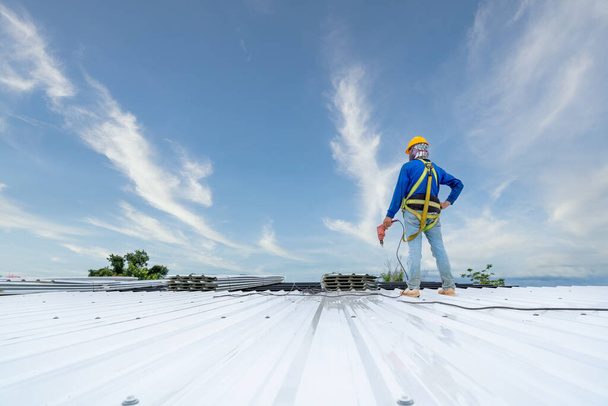 A Roofer using electric drill nail gun installing PU foam roof sheet at under construction. Safety body construction, Working at height equipment. building - Foto, Bild