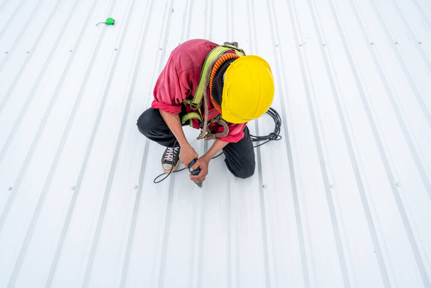 A Roofer worker using electric drill nail gun and installing PU foam roof sheet on top of the new roof, Concept of residential building under construction. - Foto, immagini
