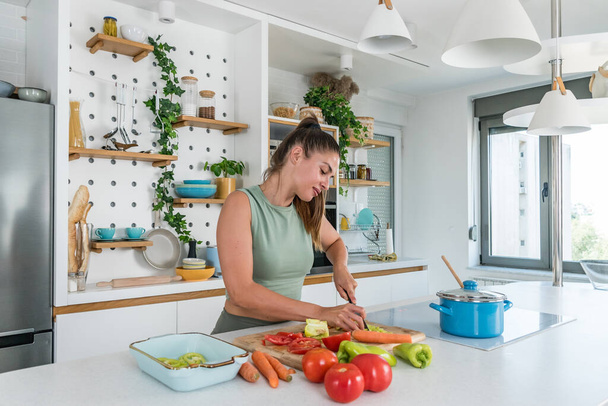 Young sporty woman cutting and cooking fresh natural vegetables at kitchen and cooking for healthy lunch. Self care yoga nutritionist girl having healthy meal after workout. - Foto, Imagem