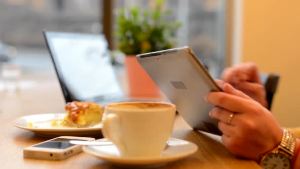 Femme travaille sur tablette au café - prise de vue à la main - ordinateur, smartphone café et gâteau en arrière-plan - rue urbaine avec des voitures en arrière-plan
 - Séquence, vidéo