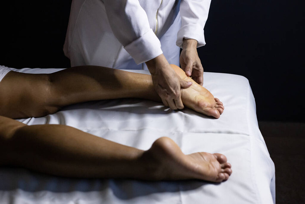 Detail of masseuse hands applying therapeutic massage on the foot of a patient who is lying on a stretcher with white sheet. - Foto, immagini