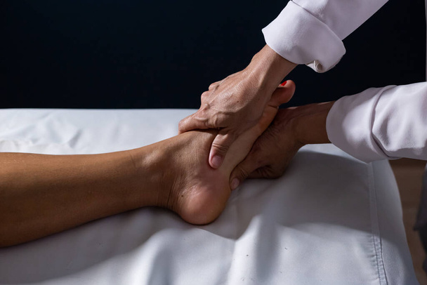 Detail of masseuse hands applying therapeutic massage on the foot of a patient who is lying on a stretcher with white sheet. - Foto, Bild