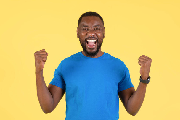 Joyful Black Guy Shaking Fists In Joy Gesturing Yes And Shouting Looking At Camera Standing On Yellow Studio Background. Millennial Man Celebrating Victory - Foto, imagen