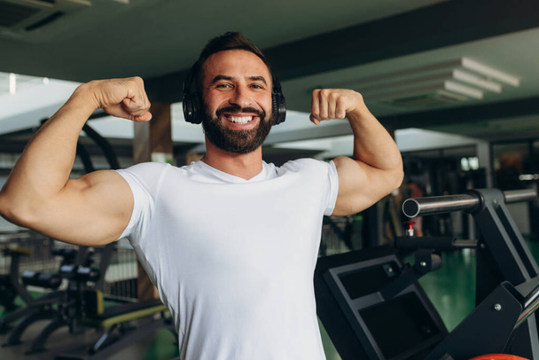 Athletic man in a white shirt shows off his muscles in the gym - Fotoğraf, Görsel