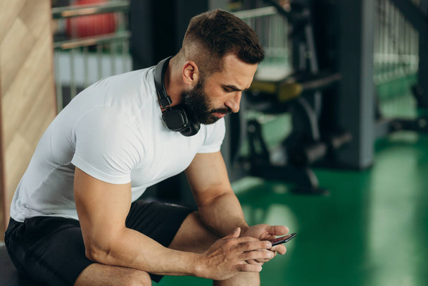 handsome man using phone while having exercise break in gym - 写真・画像