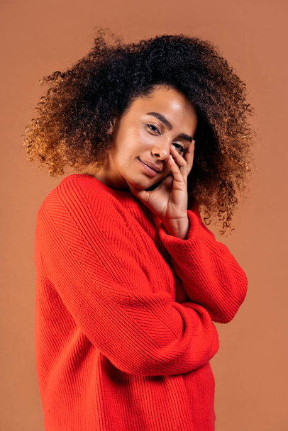 Beautiful black woman with curly hair posing and having fun in studio shot against brown background. - Фото, изображение
