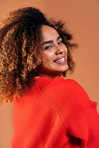Beautiful black woman with curly hair posing and having fun in studio shot against brown background. - Фото, зображення