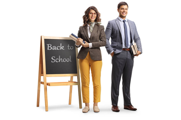 Full length portrait of a male and female teacher standing next to a blackboard with text back to school isolated on white background - Photo, image