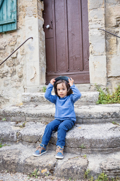 Little handsome baby boy sitting on ancient stone stairs and playing outdoor with straw hat in old city - Foto, Bild