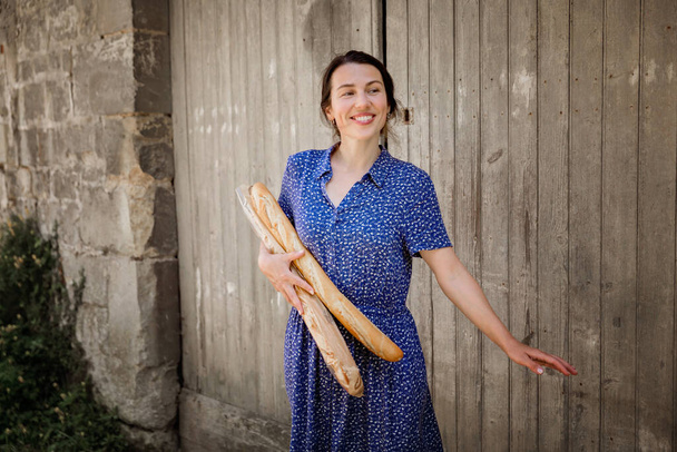 Young pretty woman standing with french baguettes in her hands in the countryside - Foto, imagen