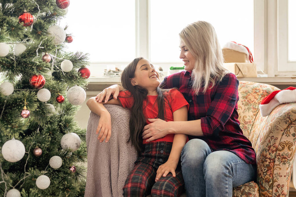 Ένα κοντινό πλάνο μιας ευτυχισμένης μητέρας που αγκαλιάζει την κόρη της, Χριστουγεννιάτικη διάθεση σε ένα άνετο σπίτι. - Φωτογραφία, εικόνα
