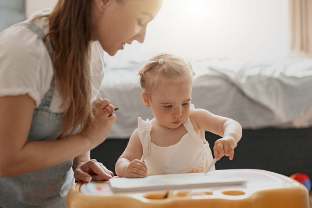 Маленькая девочка рисует со своей матерью дома, проводя время вместе. Высокое качество фото - Фото, изображение