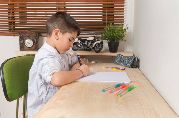 Молодий 8-річний хлопчик пише і малює на папері всередині будинку
. - Фото, зображення