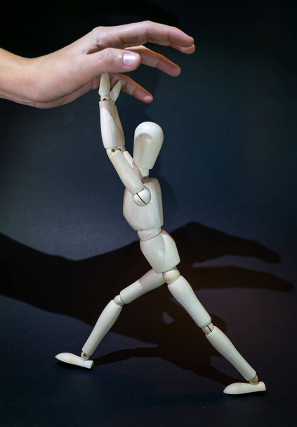 a wooden dummy fights against a human hand tryingto grasp it. black background - Foto, Imagen