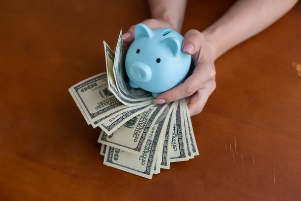 Kadın, para biriktirmek ve finansal konsept için domuzcuğa banknot dolar koyuyor. - Fotoğraf, Görsel