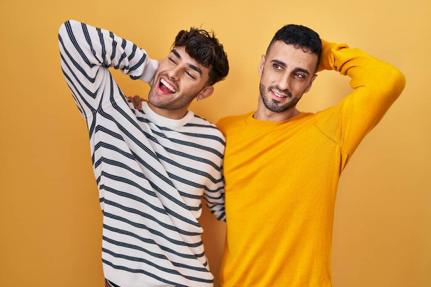 Fiatal spanyol meleg pár áll sárga háttér mosolygós magabiztos megható haj felemelt kézzel gesztus, pózol vonzó és divatos  - Fotó, kép