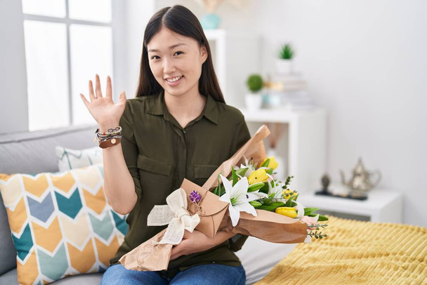 Китайская девушка, держащая букет белых цветов, отказывается сказать привет счастливый и улыбающийся, дружественный жест приветствия  - Фото, изображение