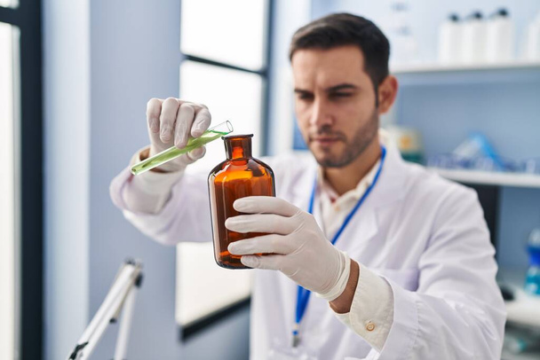Científico joven hispano vertiendo líquido en botella en laboratorio - Foto, imagen