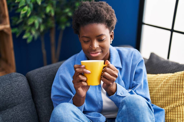 Африканська американка п "є каву, сидячи вдома на дивані. - Фото, зображення
