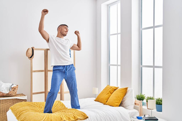 Young hispanic man dancing on bed at bedroom - Foto, afbeelding