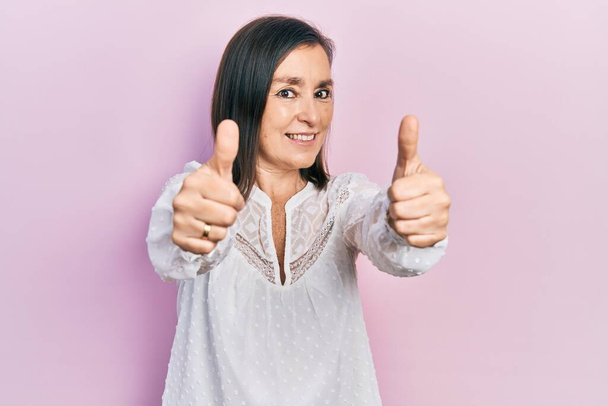Middle age hispanic woman wearing casual clothes approving doing positive gesture with hand, thumbs up smiling and happy for success. winner gesture.  - Photo, Image